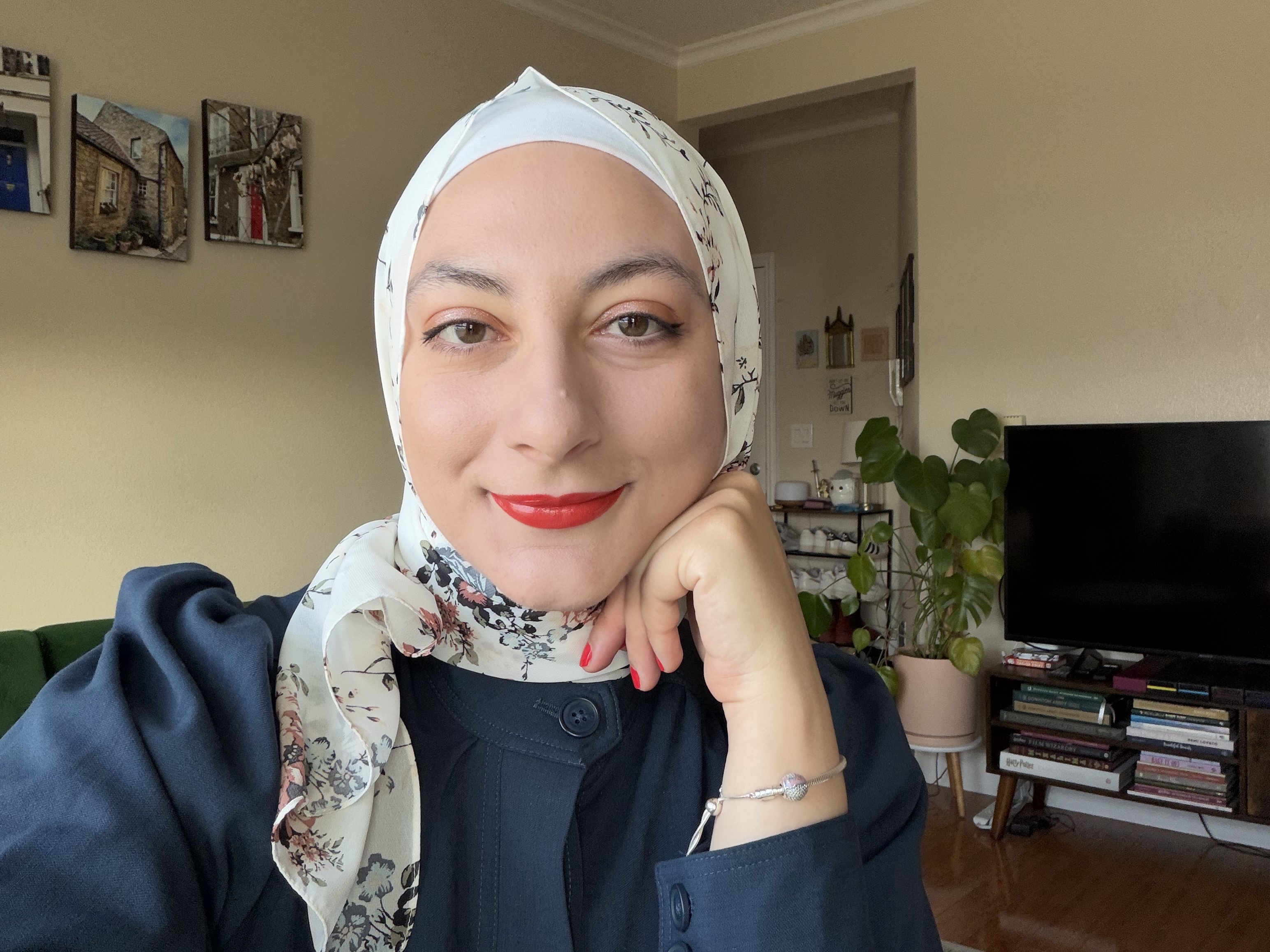 A woman in a white floral headscarf and navy shirt smiles at the camera
