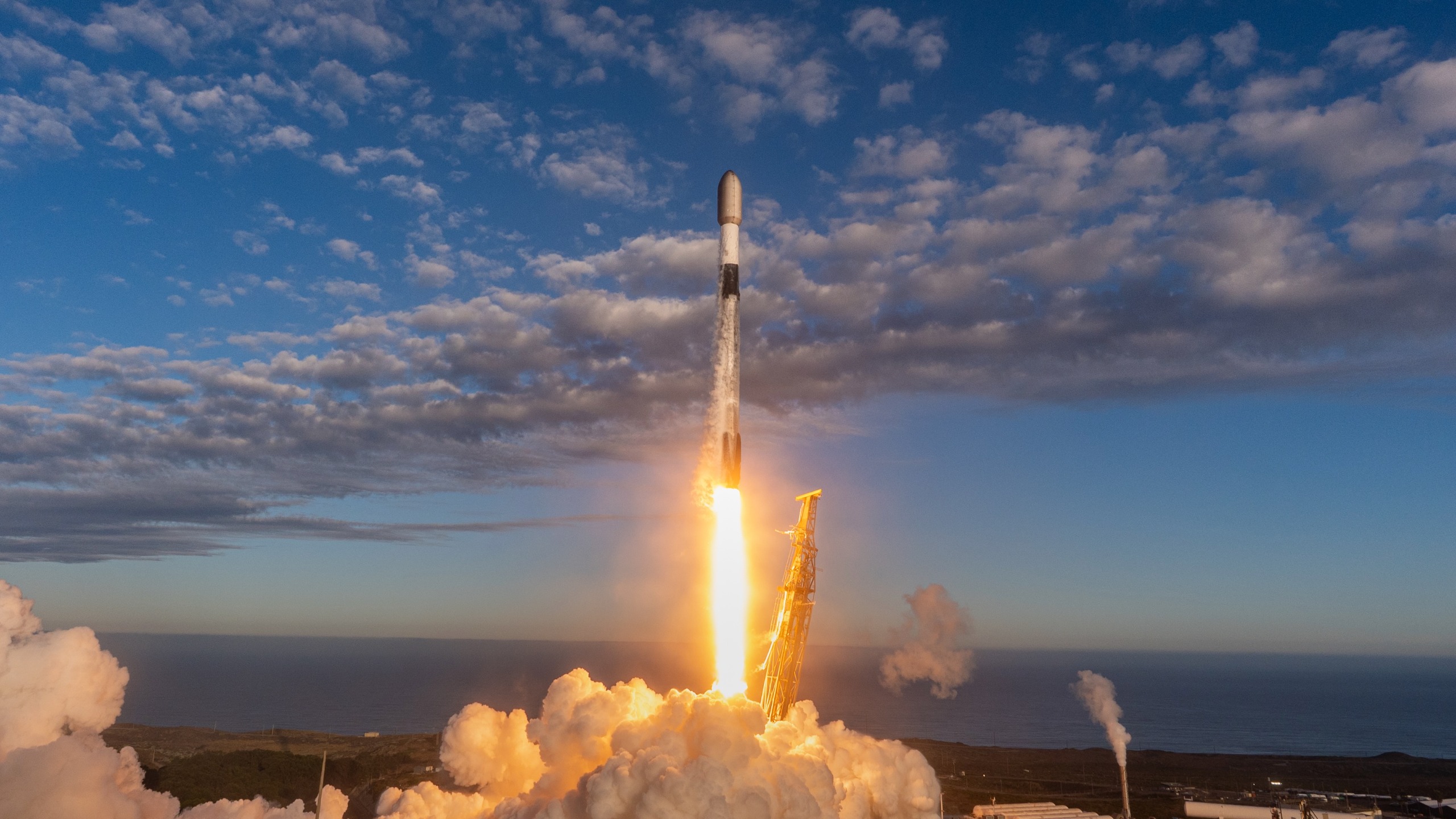 A black and white SpaceX satellite launches Starlink satellites from a seaside launch pad.