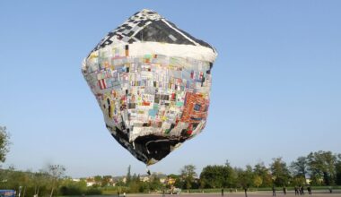 a floating artwork by Tomás Saraceno featuring a patchwork object resembling an unusual air balloon over a square