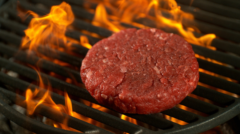 A raw burger patty on a flaming grill
