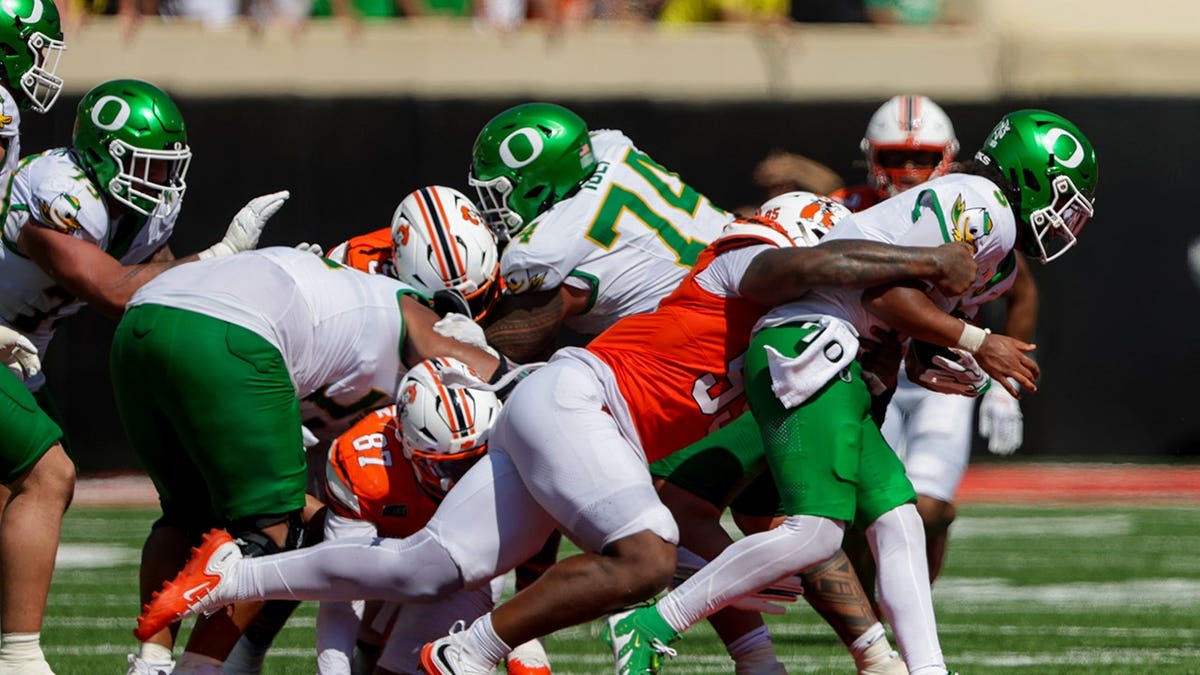 Jaleel Johnson tackles Dante Moore during an NCAA football game between Oklahoma State and Oregon.