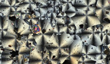 A microscopic view of the kaleidoscope-like crystal structures of two NASA-made material samples, a gray sample on the left and a reddish sample on the right.