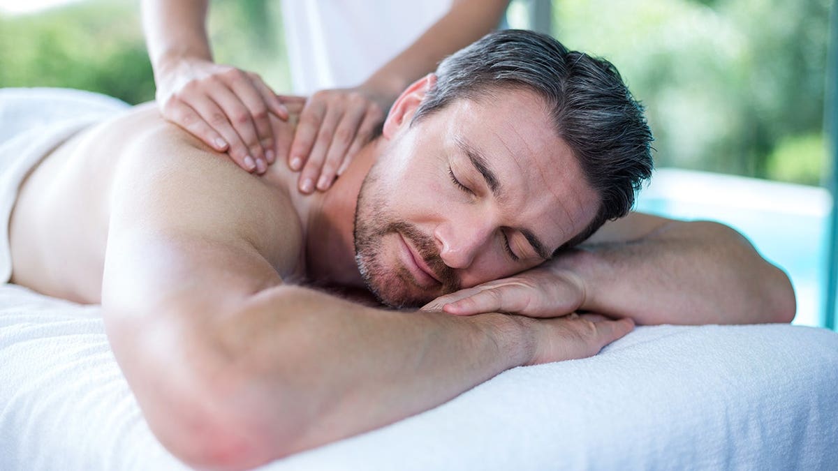 Man receives a back massage from a masseur in a spa setting.