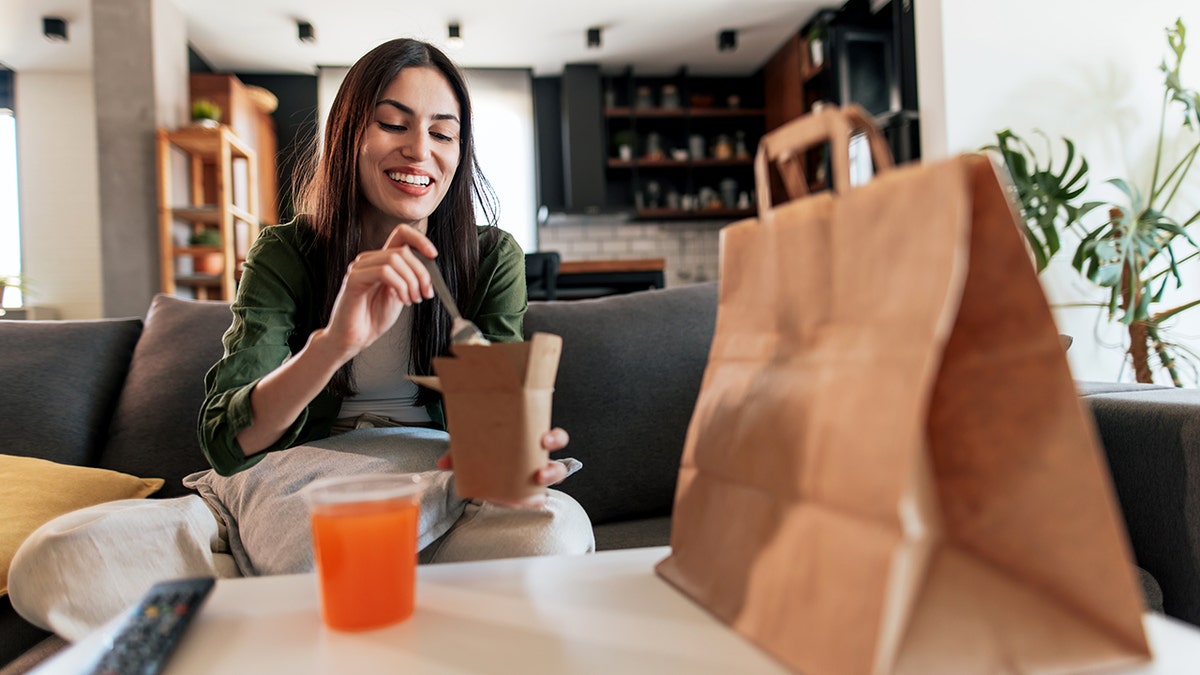 Woman enjoying takeout, ultraprocessed foods, which may link to increased mortality.
