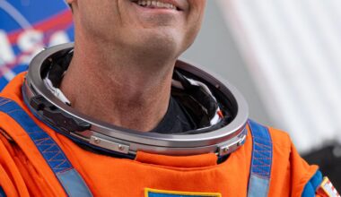 Reid Wiseman looks toward supporters, smiling, wearing an orange spacesuit with his name and a NASA meatball patch.