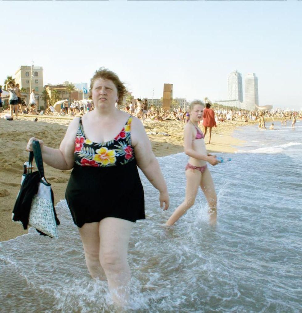A girl on a beach looking at a heavy set woman from behind.