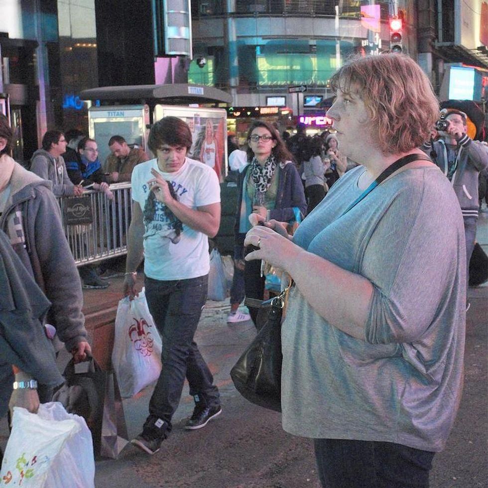 A young man in a tee shirt and jeans walking on a crowded city giving a heavy set woman a strange look.