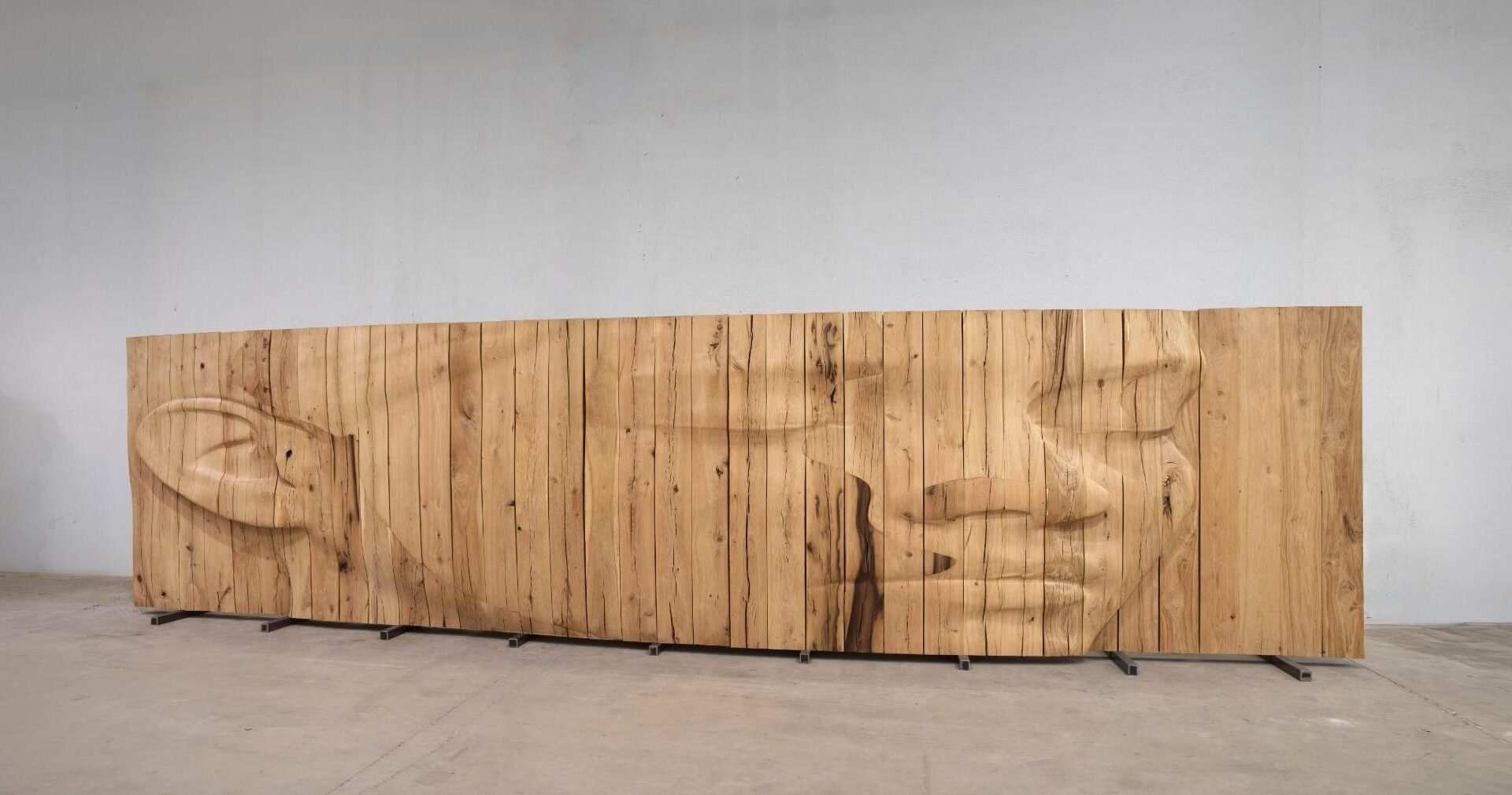 a wide wooden relief sculpture by Jaume Plensa depicting a carving of a face
