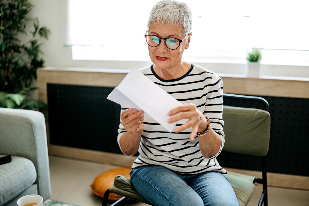 Senior woman sitting in her living room, opening mail.