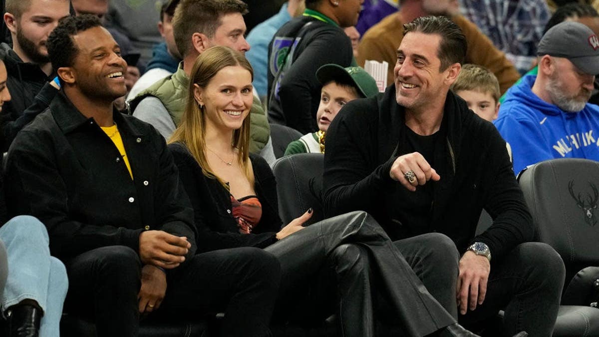 Randall Cobb, Mallory Edens and Aaron Rodgers seated watching a basketball game.