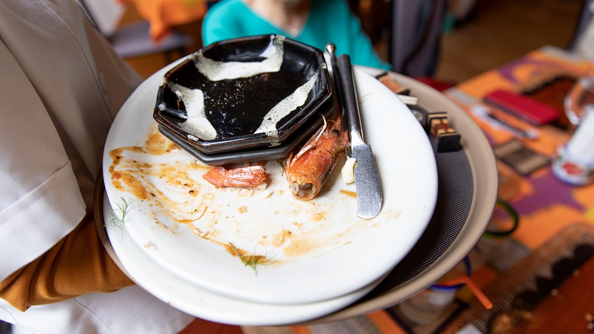 A restaurant server holds a stack of dirty plates over a table.