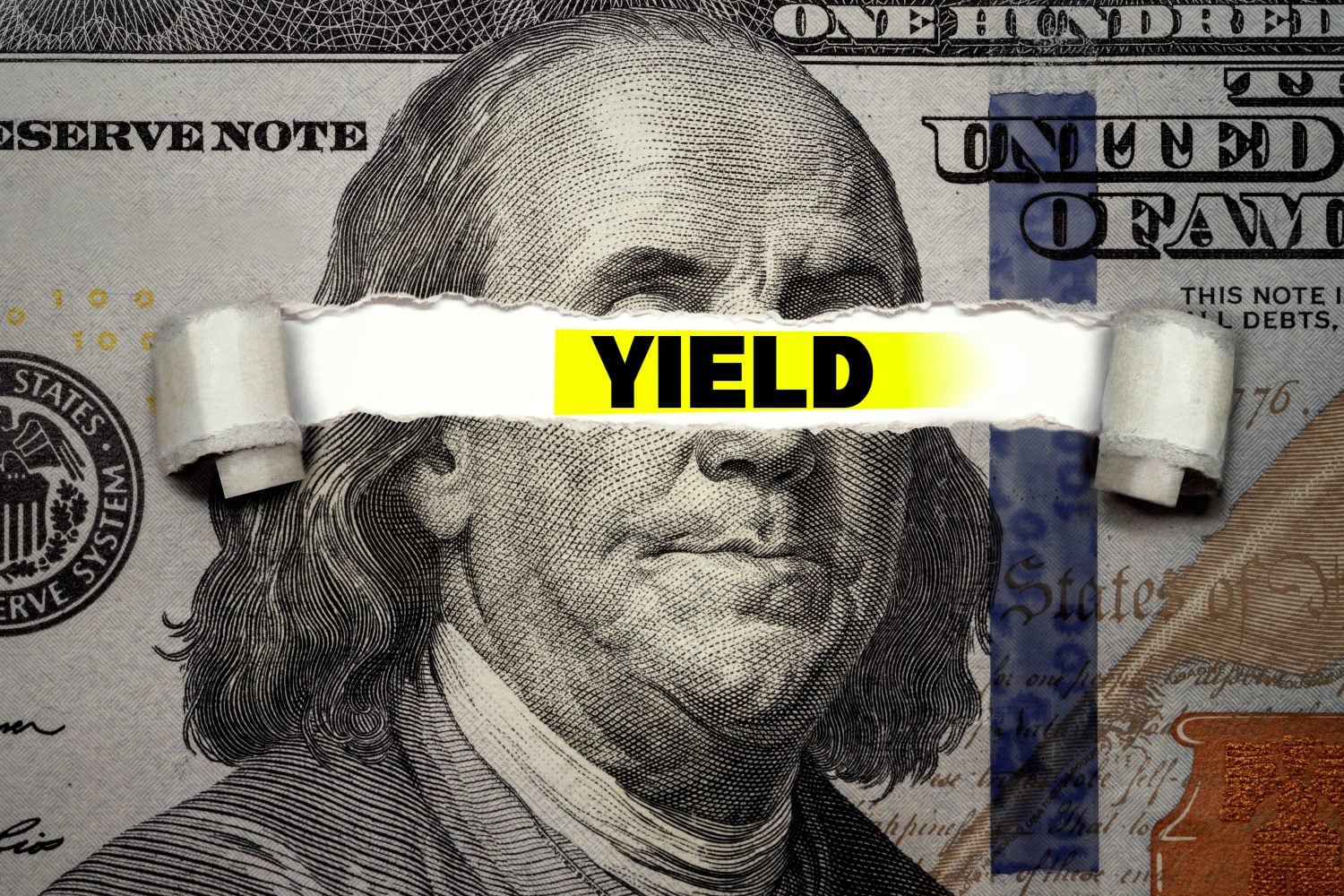 A close-up of a U.S. hundred-dollar bill, showing Benjamin Franklin's face. A horizontal tear rips across the center of the bill, revealing a vibrant yellow background with the word "YIELD" prominently displayed in bold black capital letters. The torn edges of the paper curl slightly inwards.