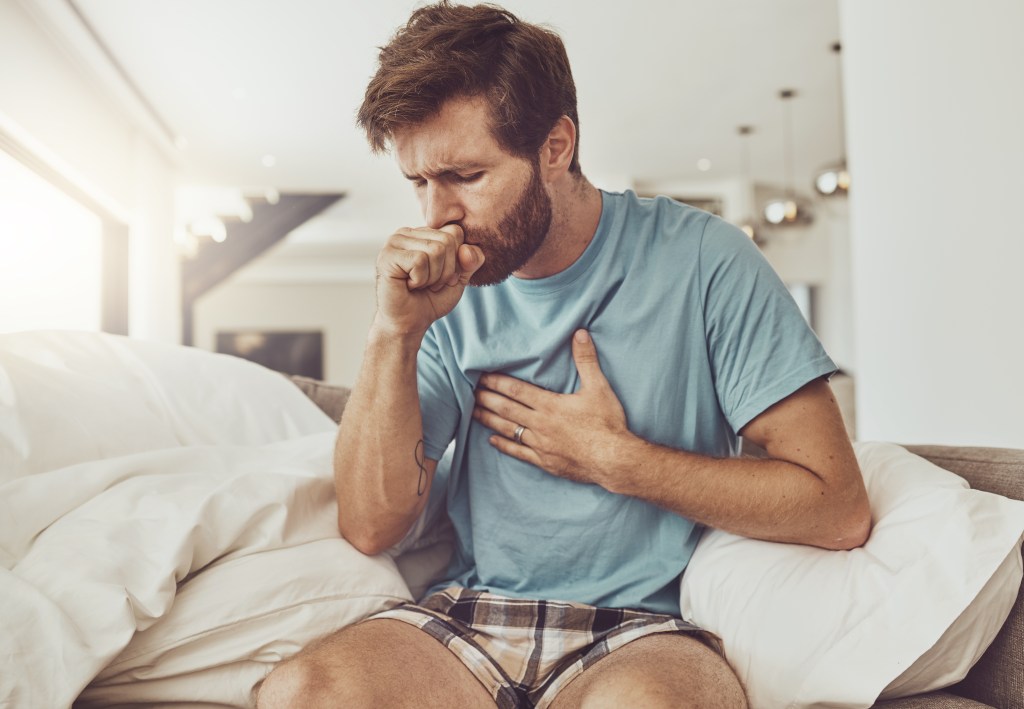 A man on a sofa coughing with chest pain.