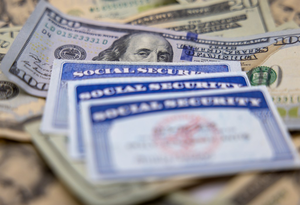 Three Social Security cards resting on a pile of US dollar bills.