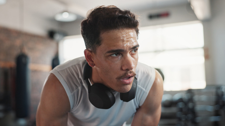 A sweaty man at the gym, with headphones around his neck.