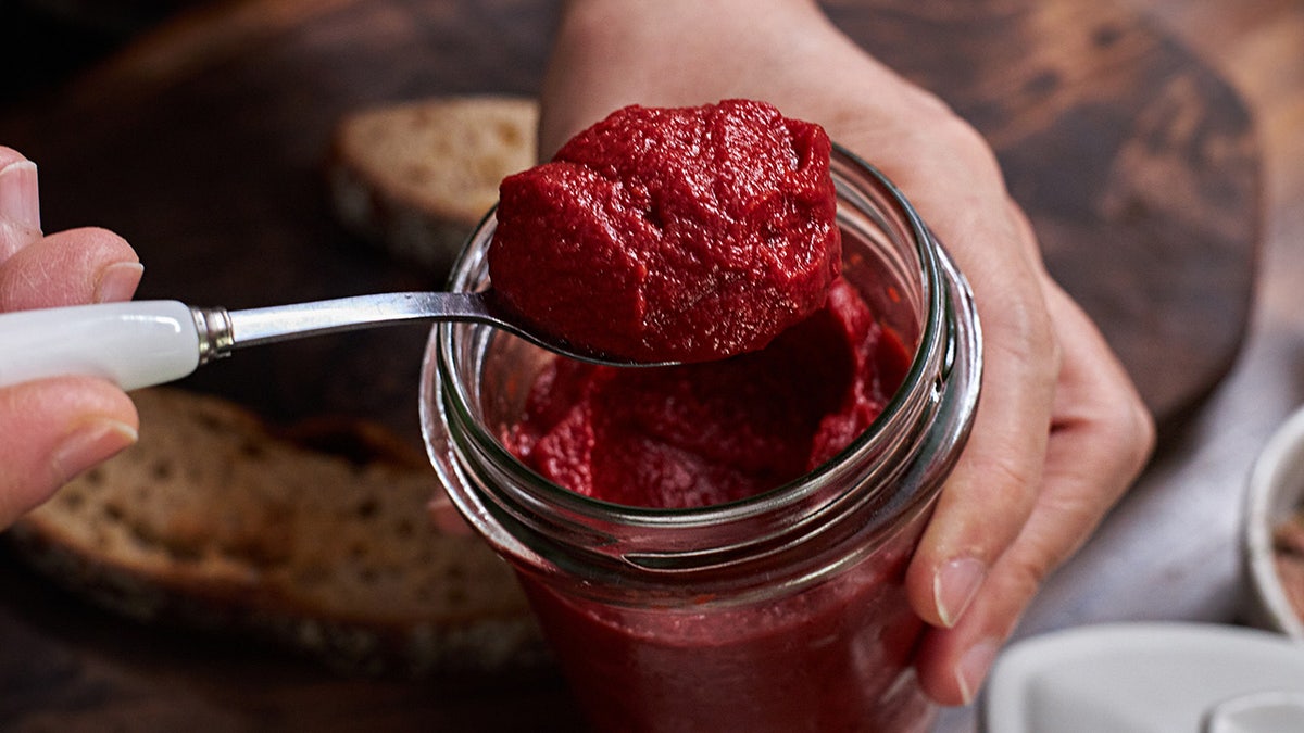 Hands holding glass jar of tamto paste, scooping out with a spoon