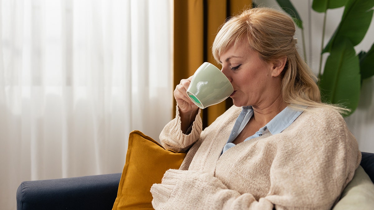 Woman relaxing on a couch while drinking a hot beverage from a mug at home.