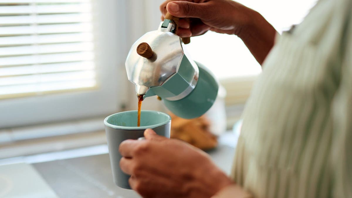 A woman pours coffee from a French press into a cup.