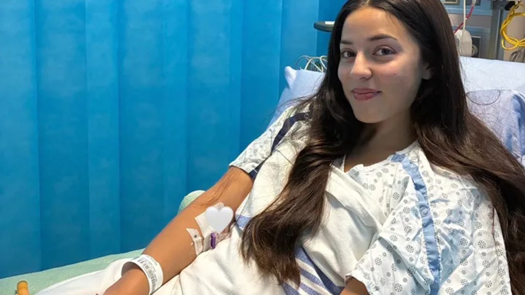Milaria Okabe in a hospital bed with an IV in her arm.