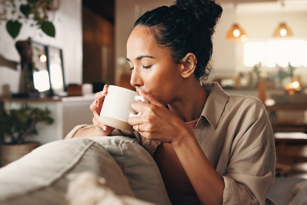 A woman sitting on a couch drinking coffee from a mug at home.