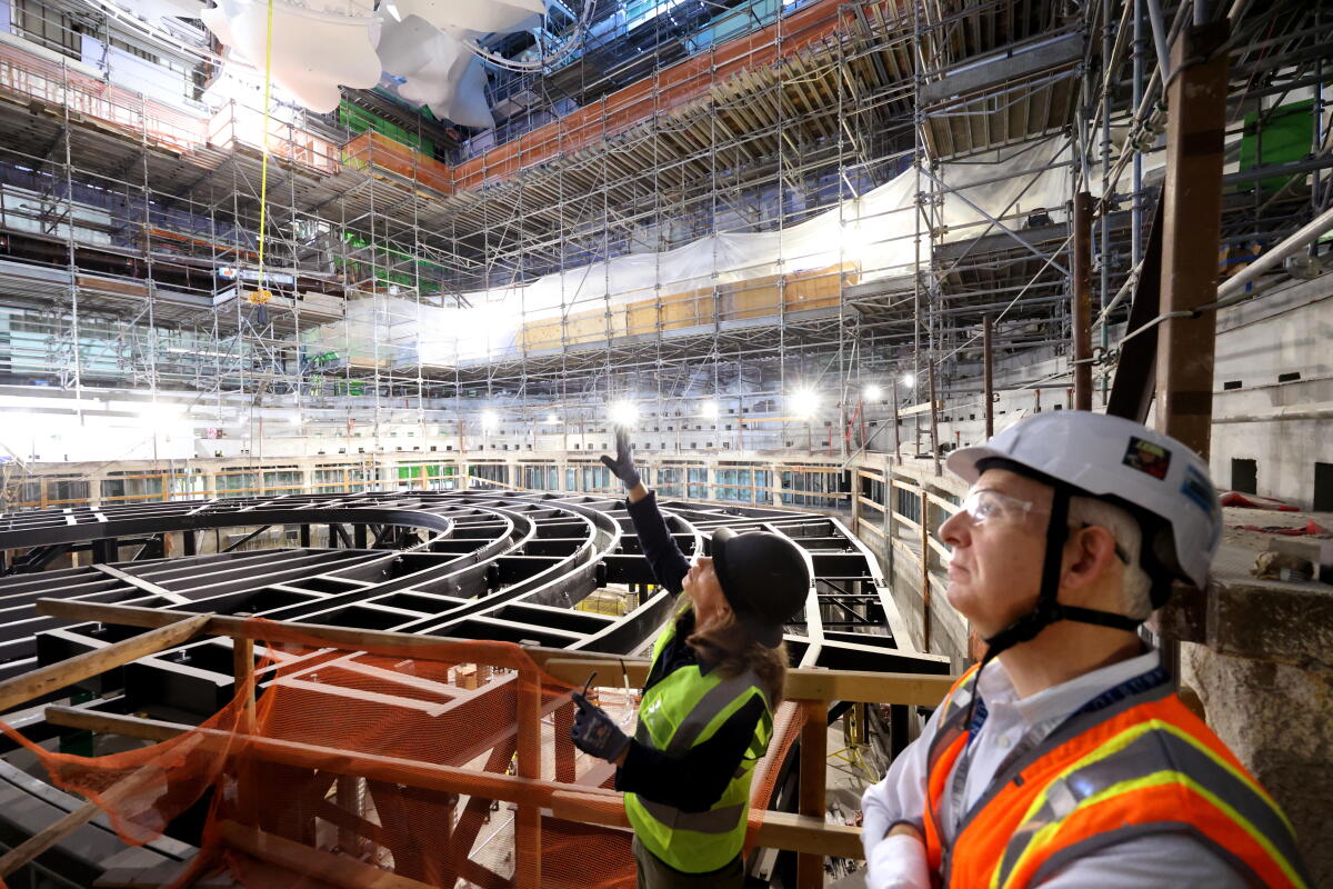 Two people in hard hats look at a concert hall under construction.