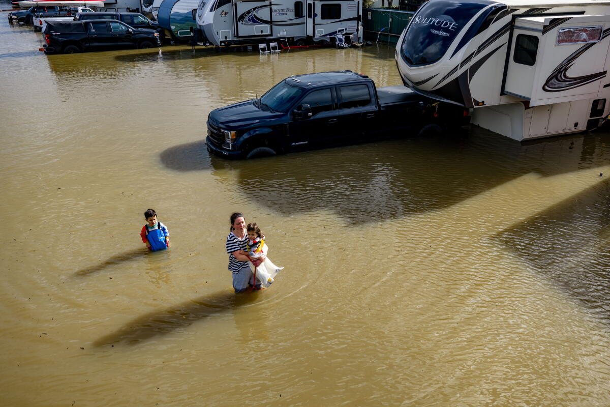 People wade through floodwater, near parked cars