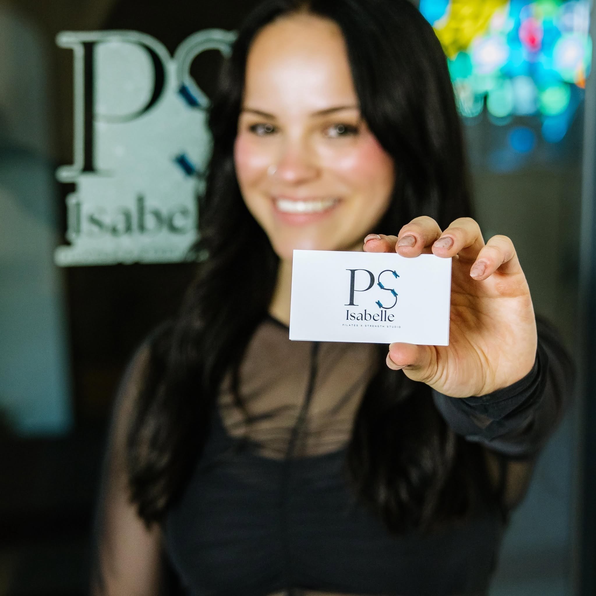 Isabelle Braun, owner of  Pilates & Strength Studio by Isabelle, also known as P.S. Isabelle, holding her business card while standing in front of her business. Courtesy photo from Facebook. 