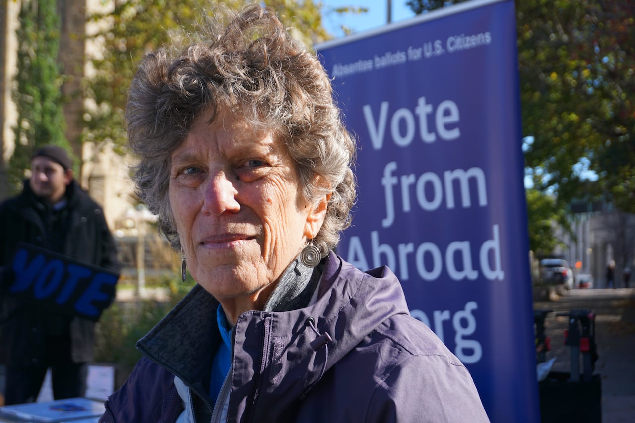 A photo of a woman with a "vote from abroad" sign behind her