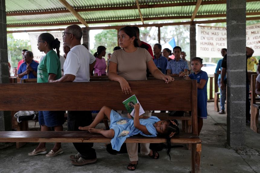 Josy Sanchez plays with a book as her mother, Maricel Sanchez, attends a Mass before a pilgrimage ahead of planned exhumations as part of the resettlement process for the Rio Indio reservoir project, in El Limon, Colon province, Panama, on July 26.