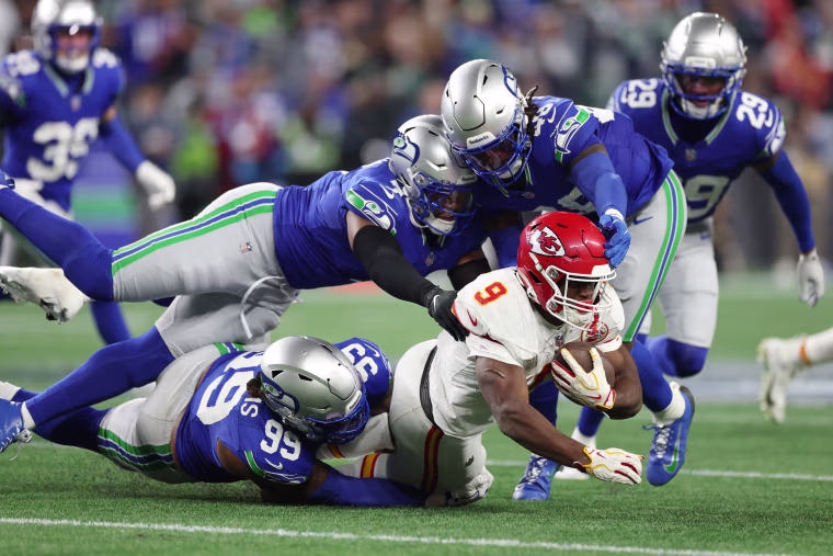 Chiefs running back Kenneth Walker III is tackled by Leonard Williams, Uchenna Nwosu and Tyrice Knight of the Seahawks.