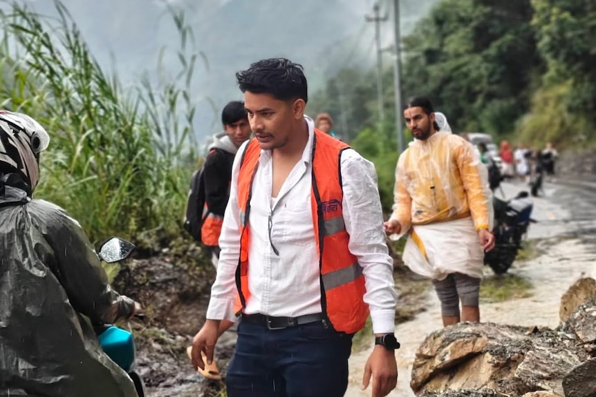 A man in high vis stands on a road, helping people.