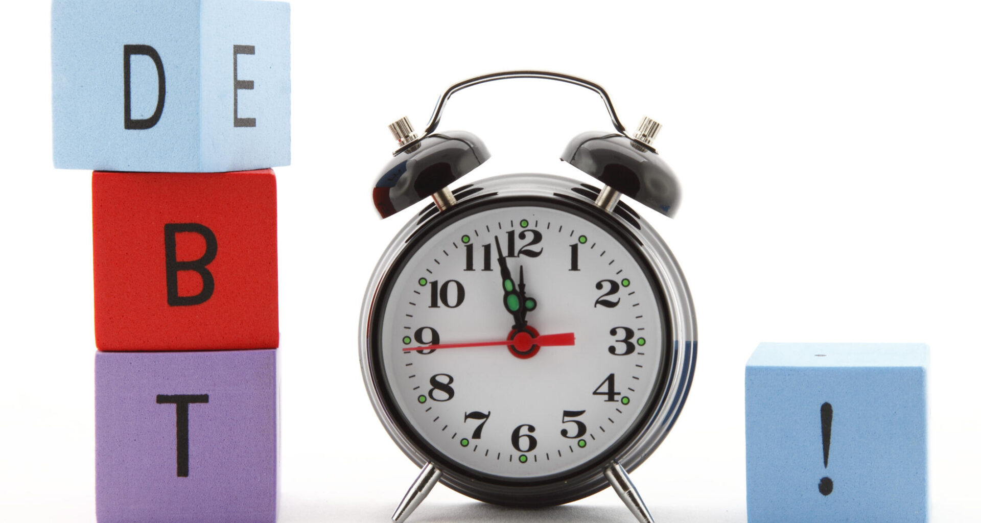 A photo of an alarm clock with multicolored building blocks on either side of it. The three blocks on the left side spell out "D" "B" "T" and the one on the right has an exclamation point on it.