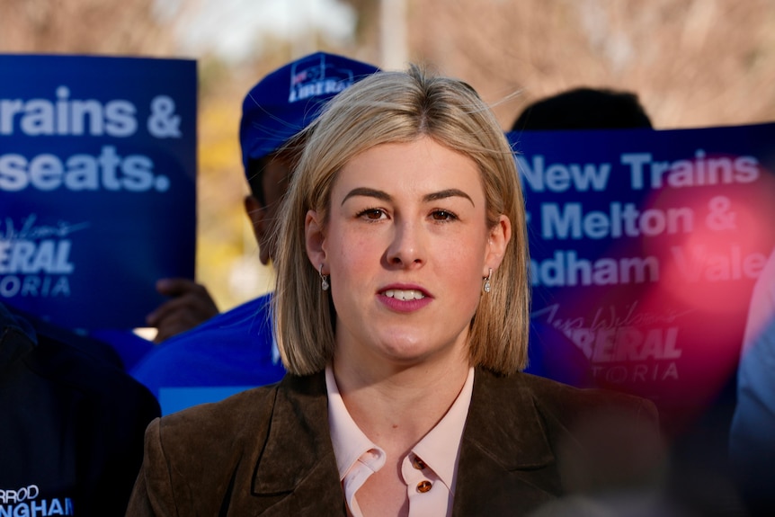 A woman speaks in front of blue placards at a press conference.