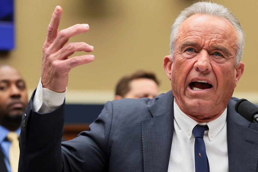 Robert F Kennedy Jr in a dark suit and tie speaking emotively with his right hand raised.