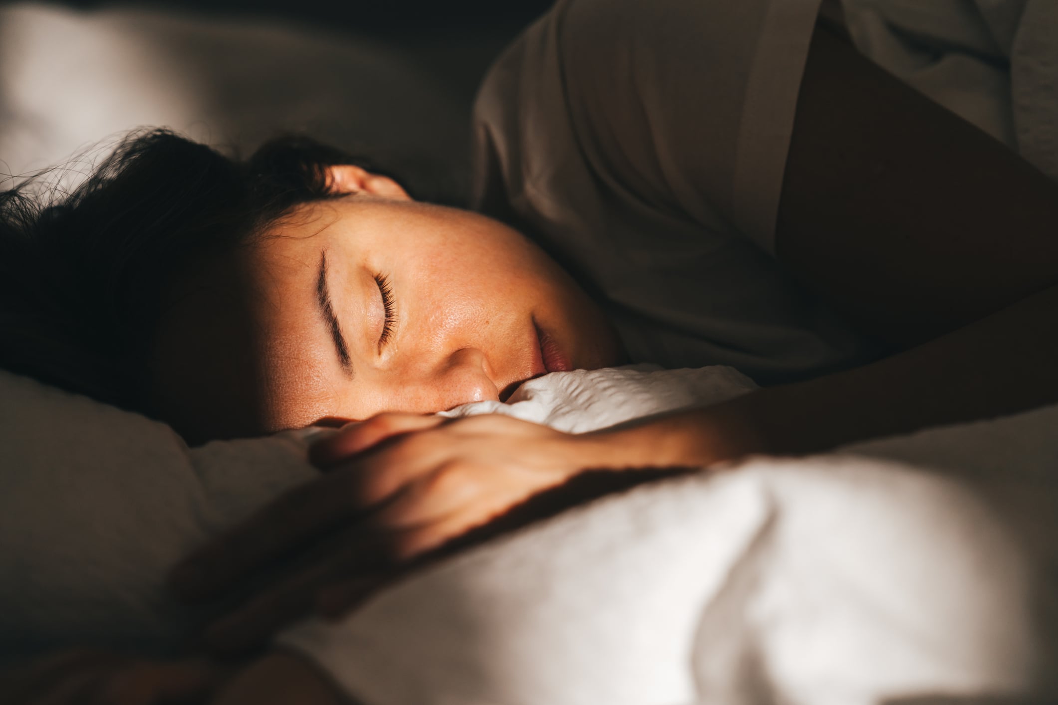 Close-up photo of a deep-sleeping woman with golden sunlight on her face.