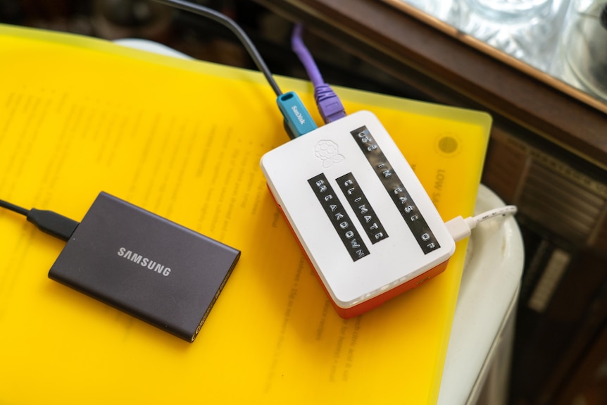 A raspberry pi, asmall white box the size of an average hard drive, sits on a pile of documents on a stool