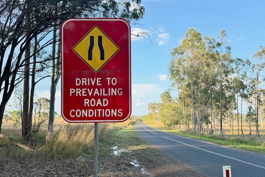 A red road sign reading  "drive to the prevailing road conditions".