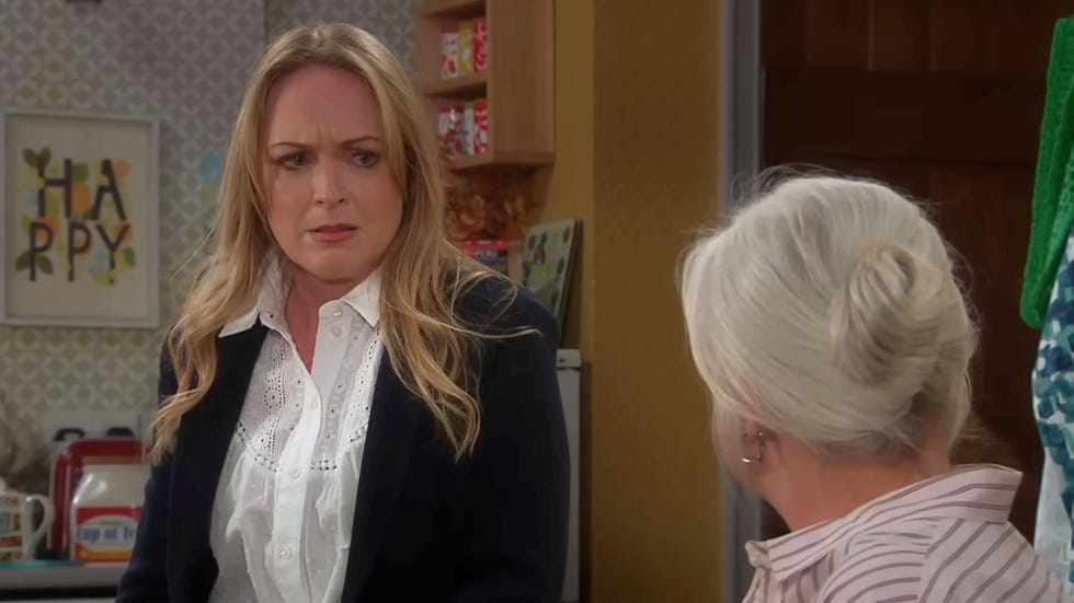 Emmerdale Vanessa Woodfield and Dr Caitlin Todd emmerdale, living room, vanessa woodfield wearing a black blazer over a white shite, standing up and looking shocked while dr caitlin todd is sat down, facing her with her back to the camera