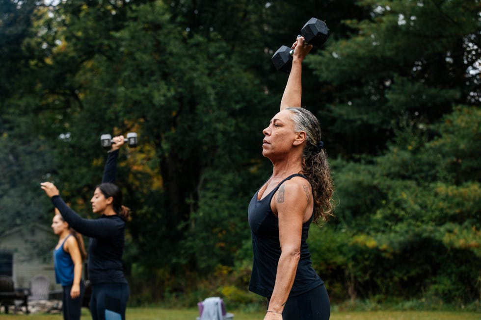 Mature woman working out with dumbbells during outdoor fitness class Mature woman working out with dumbbells during outdoor fitness class