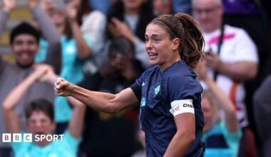 Alexia Putellas celebrating a goal with a clenched right fist as fans show their excitement in the background, raising their arms and applauding