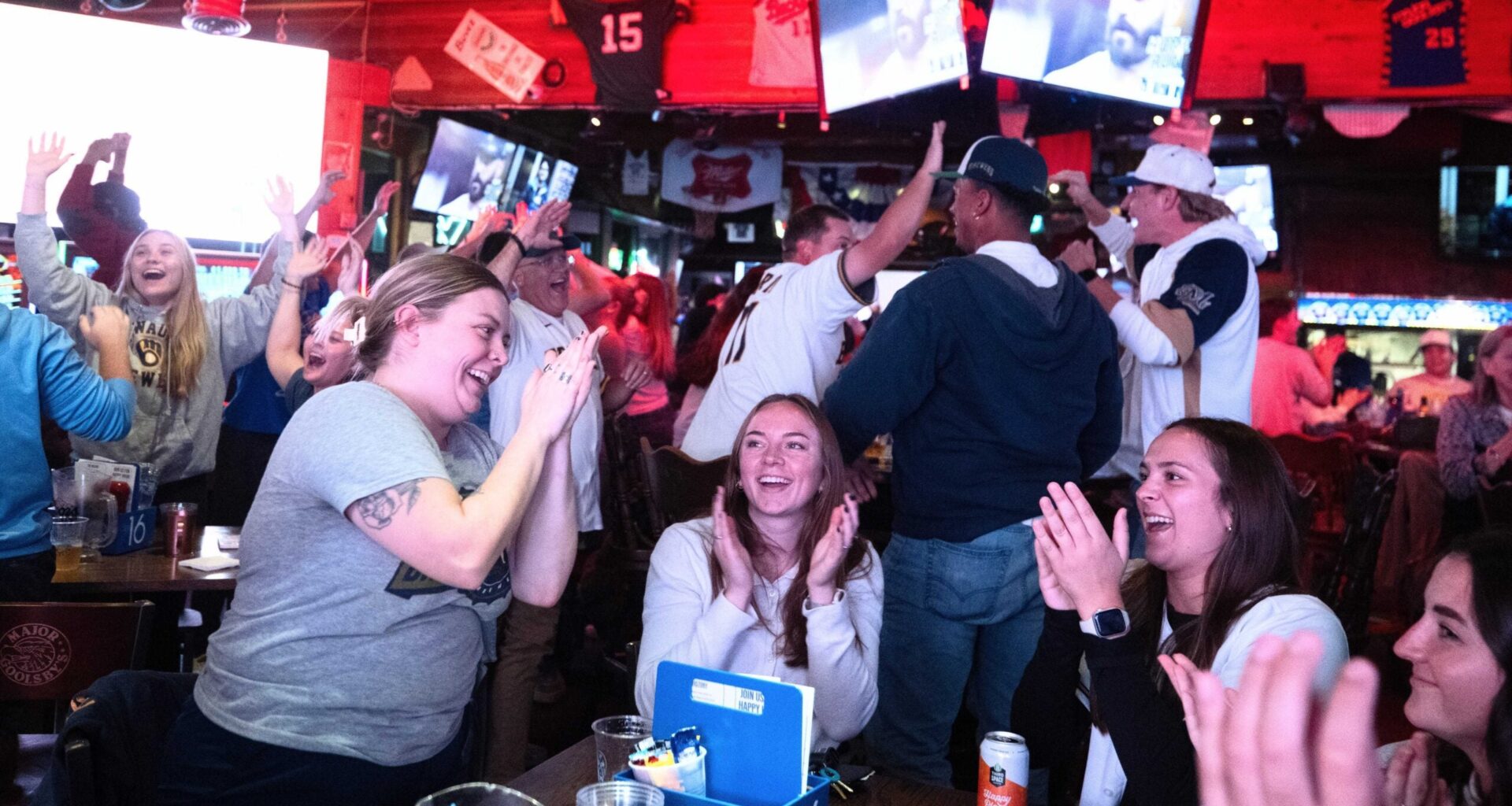 A group of people in a sports bar cheering and clapping while watching a game on multiple television screens.