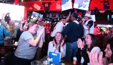 A group of people in a sports bar cheering and clapping while watching a game on multiple television screens.