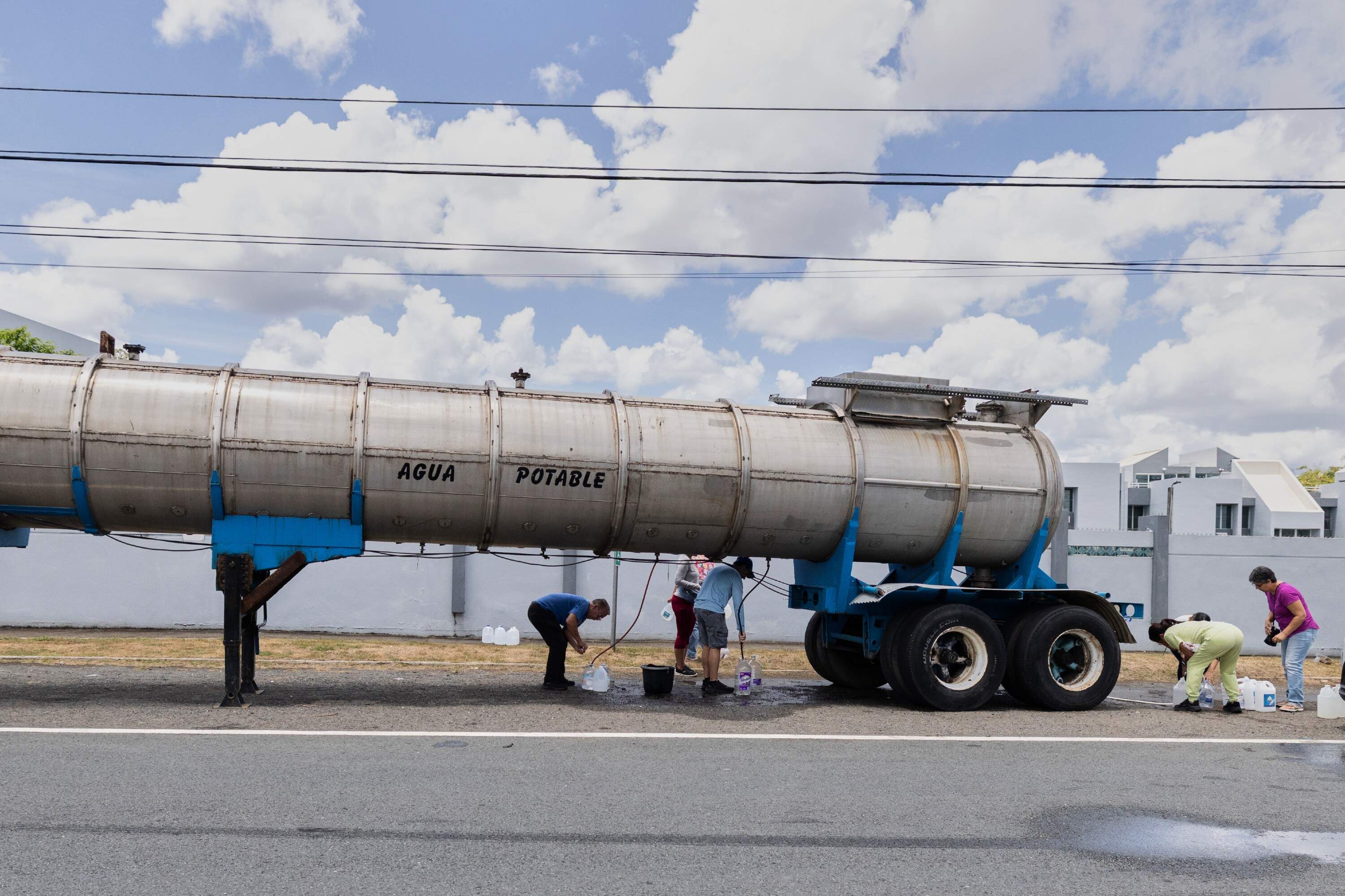 A water tanker truck marked "Agua Potable" is parked roadside as residents fill containers with water amid ongoing rationing, in San Juan, Puerto Rico, on Aug. 5. (Alejandro Granadillo)