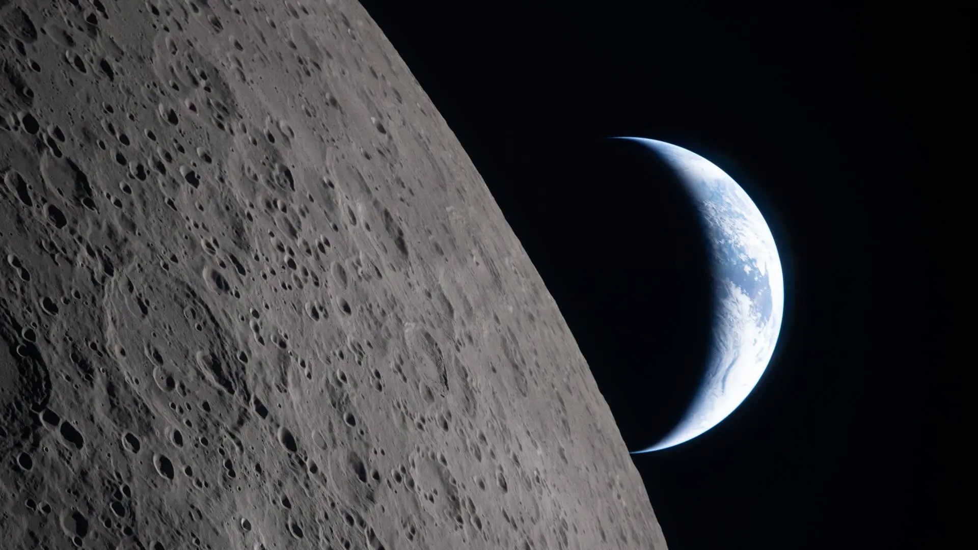 photo from a spacecraft flying around the moon, showing a crescent earth beyond the lunar limb