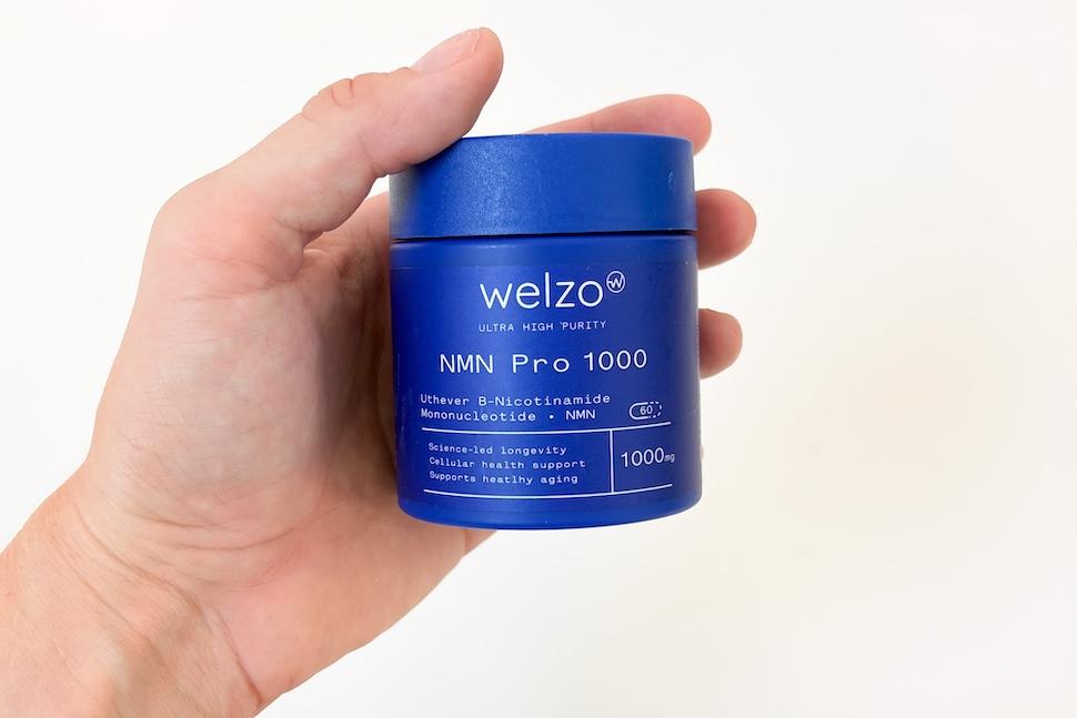 Closeup of a hand holding a canister of Welzo Ultra Purity NMN Pro 1000