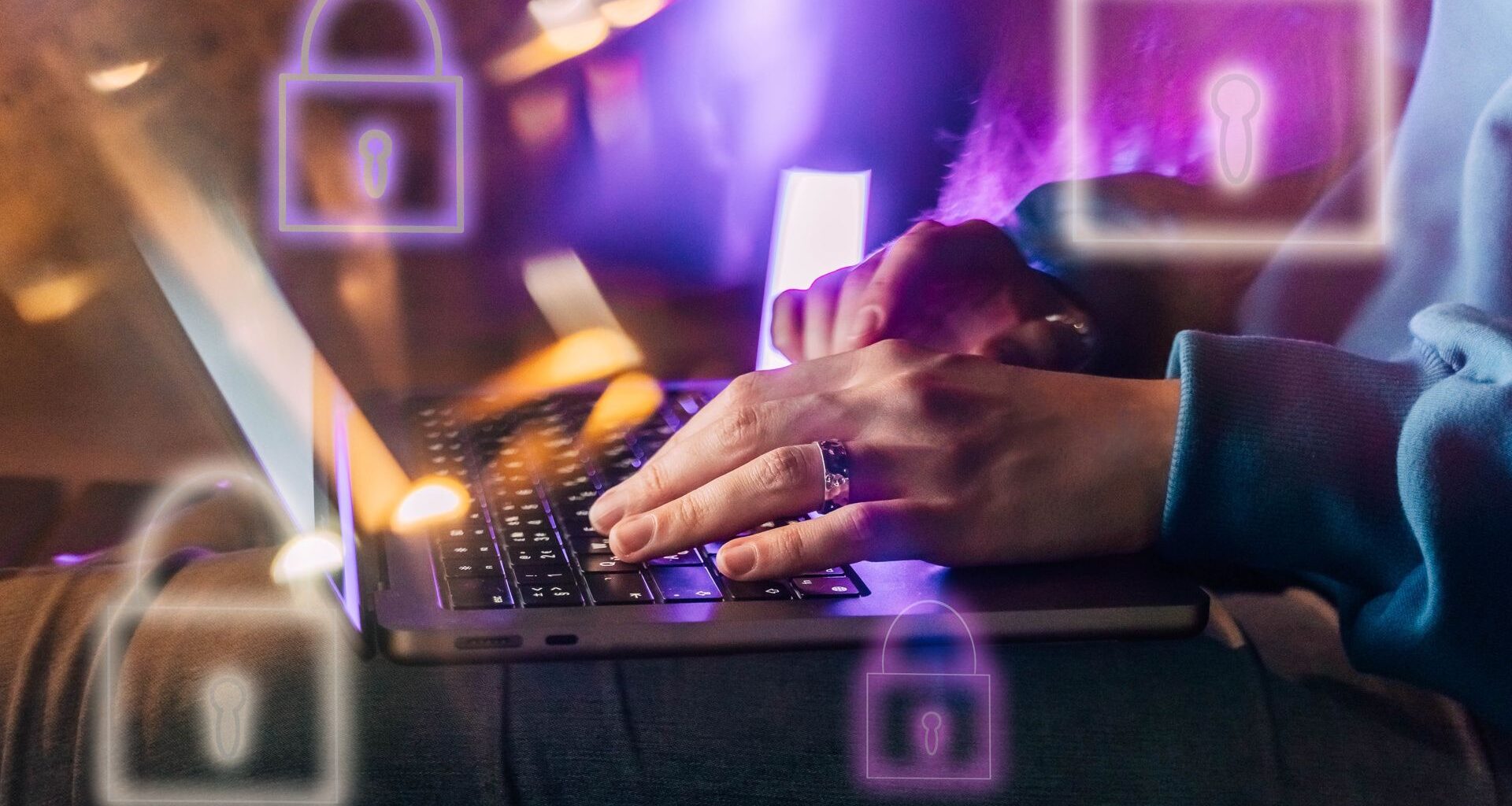 Female hands typing on a laptop in neon light. A lock as a symbol of cybersecurity on a foreground.