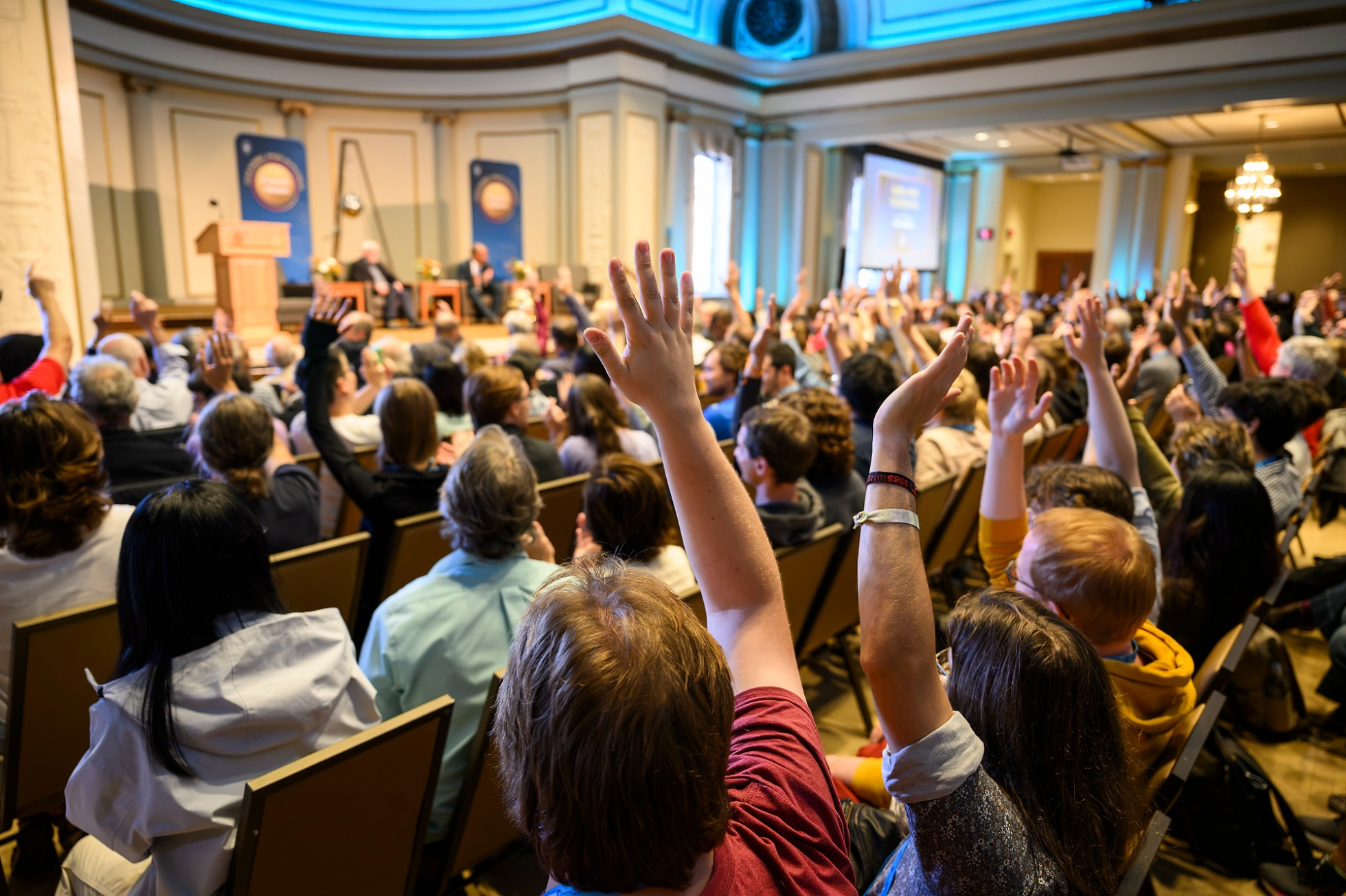 A seated crowd at the Nobel Prize celebration with many hands raised