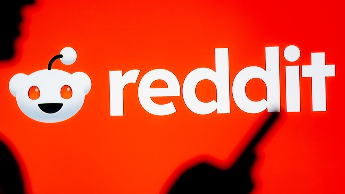 In this photo illustration, a woman seen looking at a smartphone with a Reddit logo displayed.