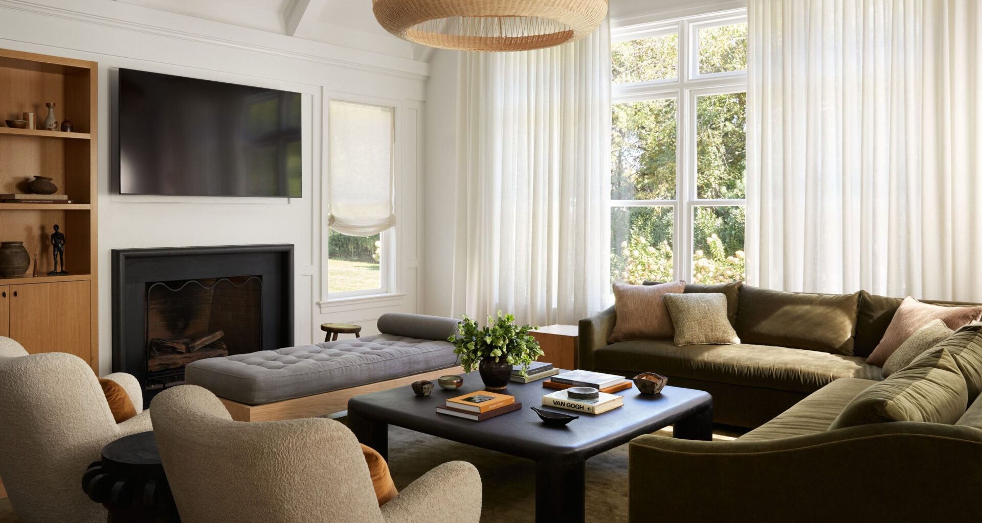 White living room with olive green velvet corner sofa, two beige armchairs, black square coffee table, grey ottoman and black fireplace
