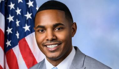 A man smiles in a suit in front of an American flag